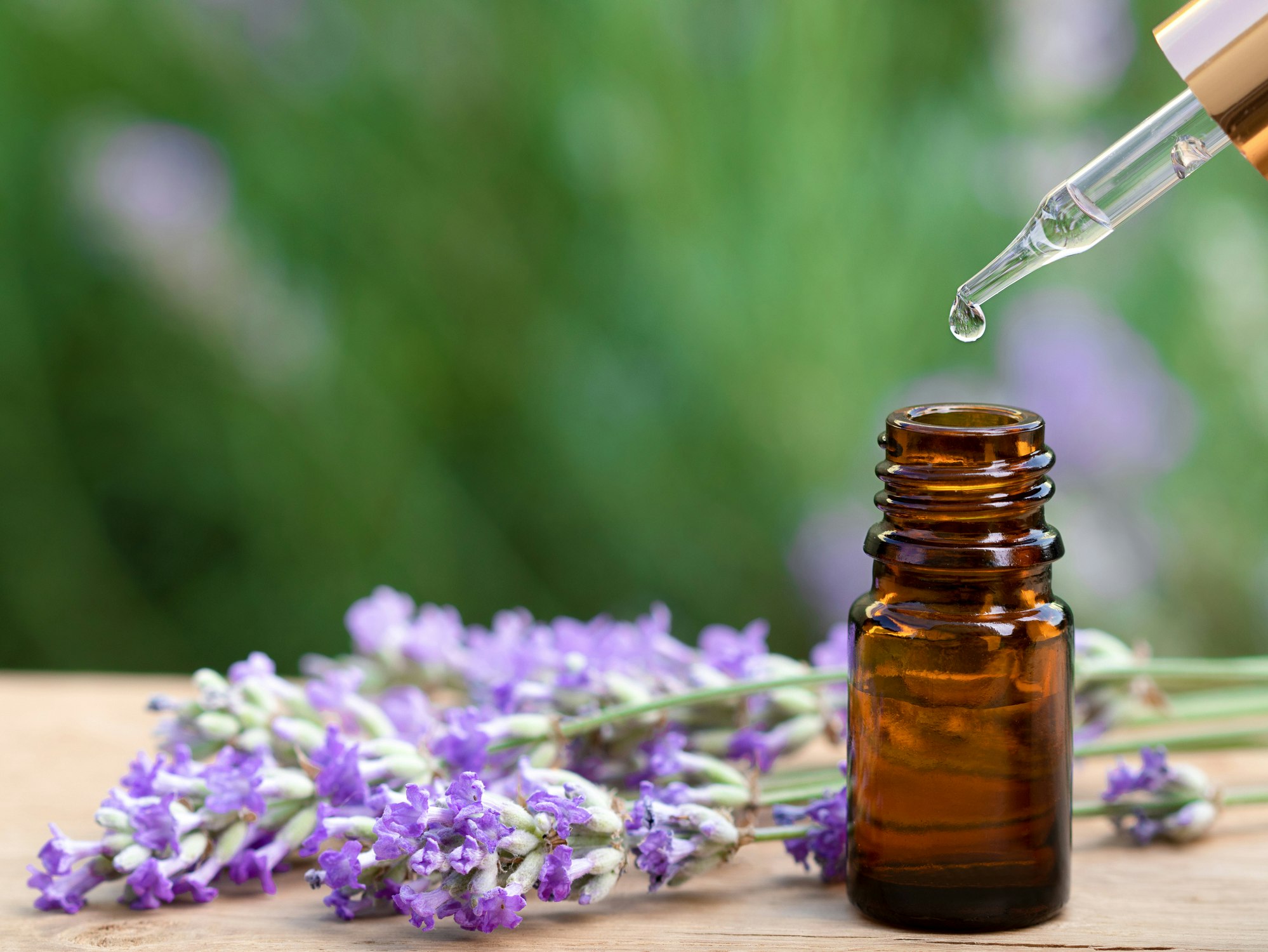 Photo of a glass bottle with lavender oil and Lavender on the wooden desk