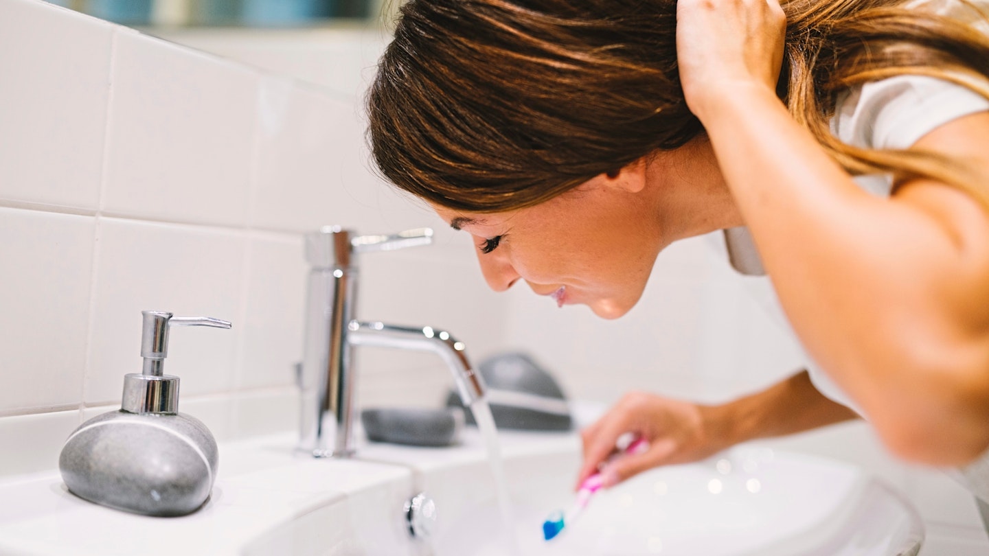 Woman washing mouth with water after brushing her teeth