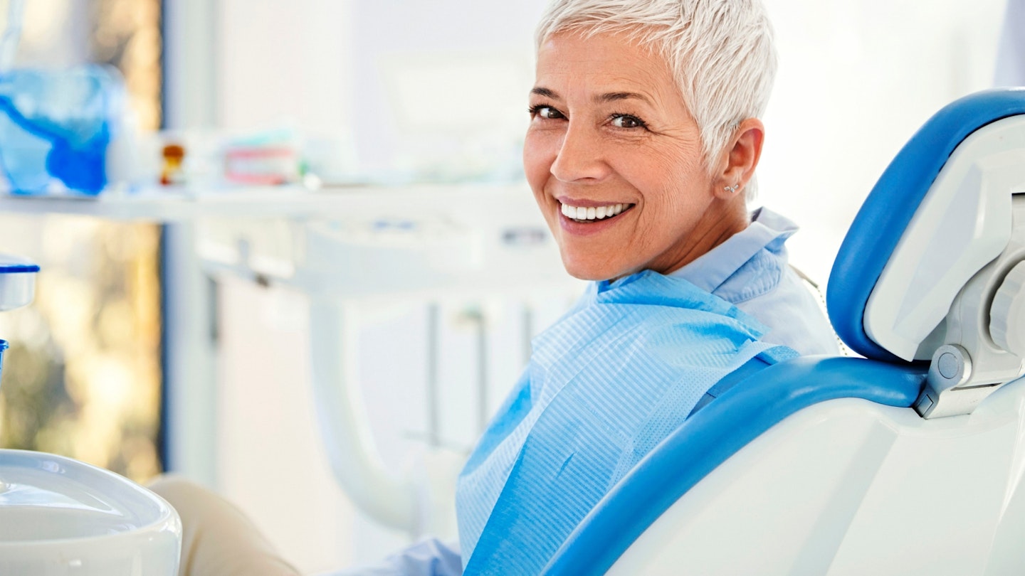 Closeup over the shoulder view of a cheerful mid 50's female patient happily smiling to the camera aftersuccessful dental procedure.