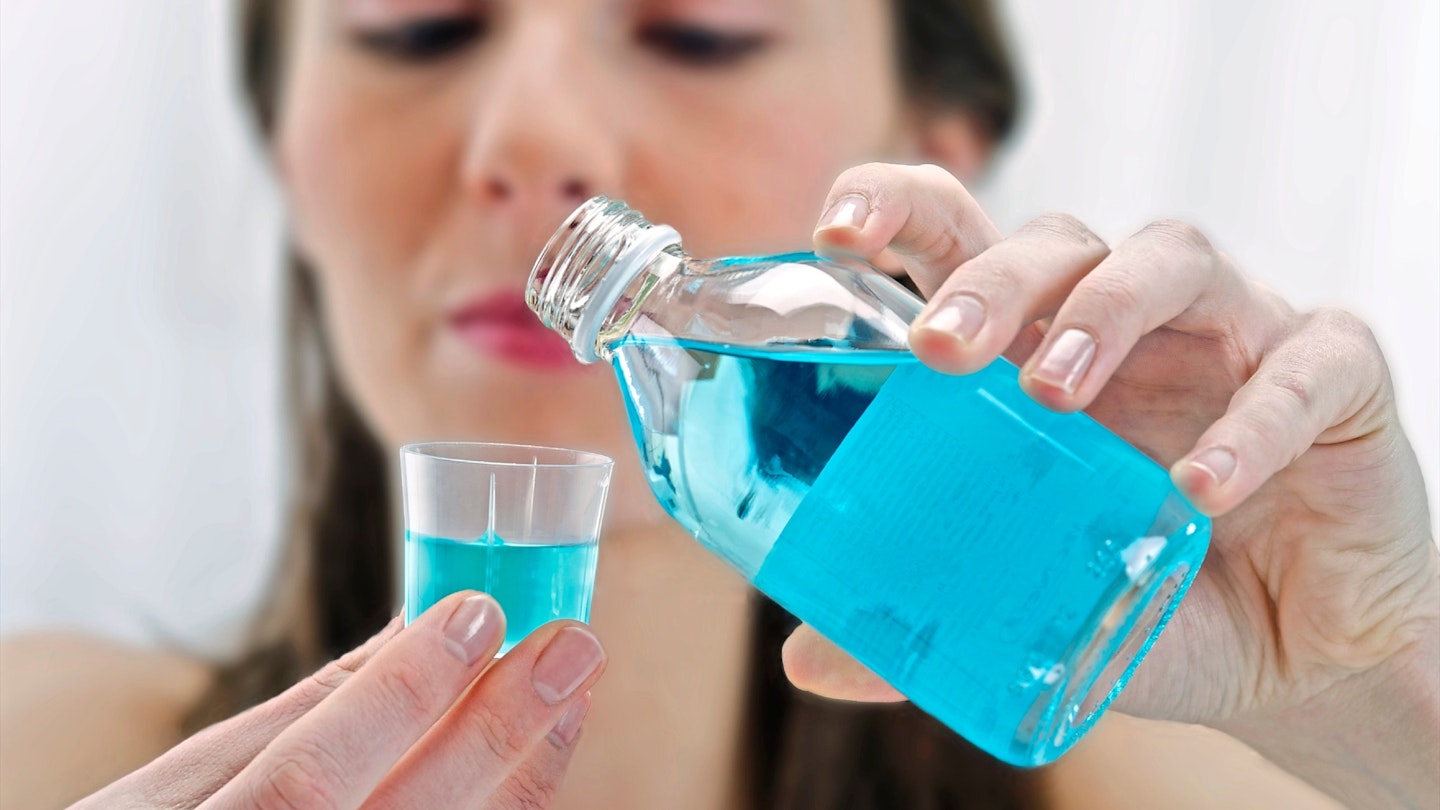 Woman carefully pouring blue mouthwash into a cup.