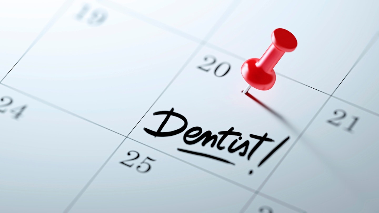 a Calendar with a red push pin next to the words Dentist! written on a white notebook to remind you an important appointment.