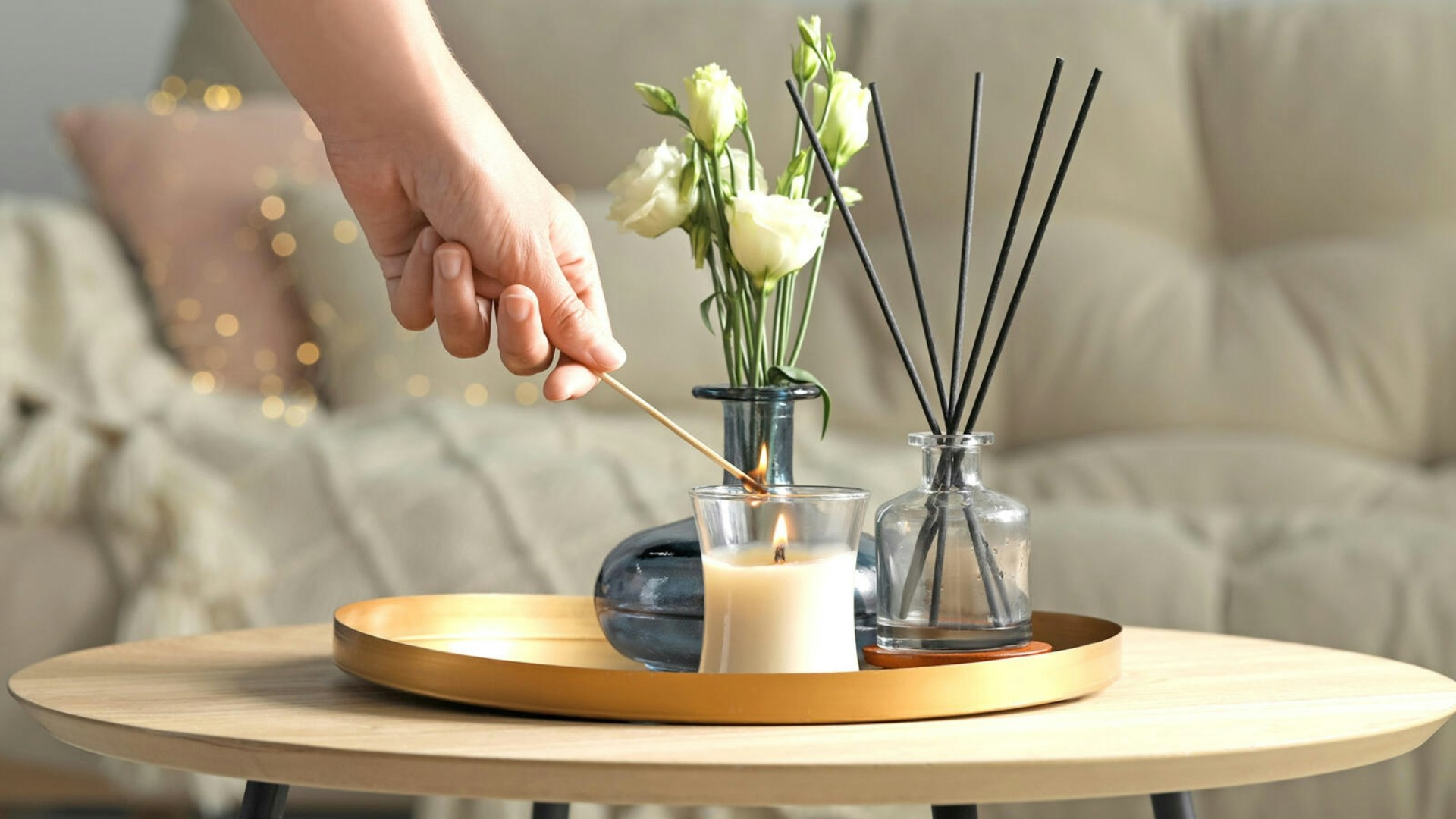 Someone lighting a candle with a match with some flowers and reed diffuser in the background