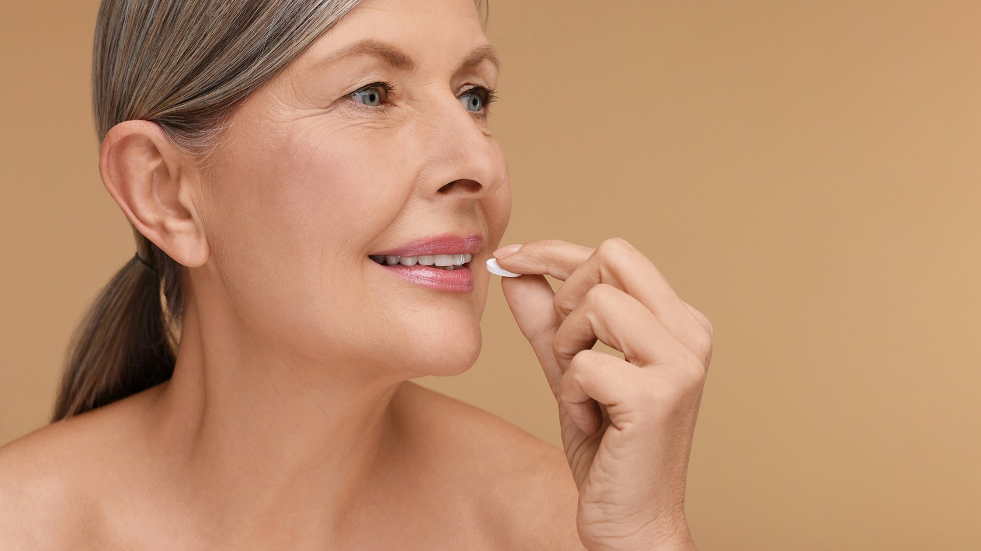 Beautiful woman taking vitamin pill on beige background