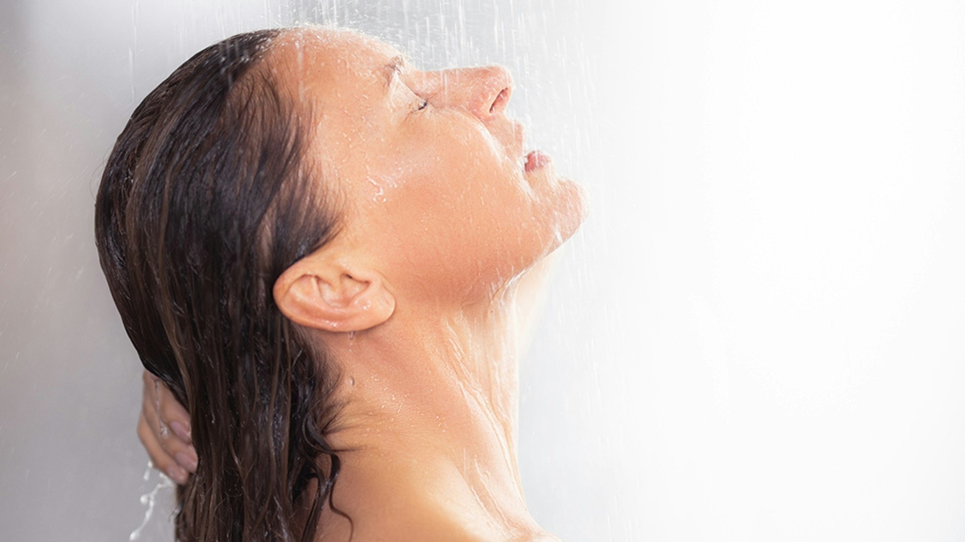 Side view portrait of attractive woman standing under water drops at bathroom