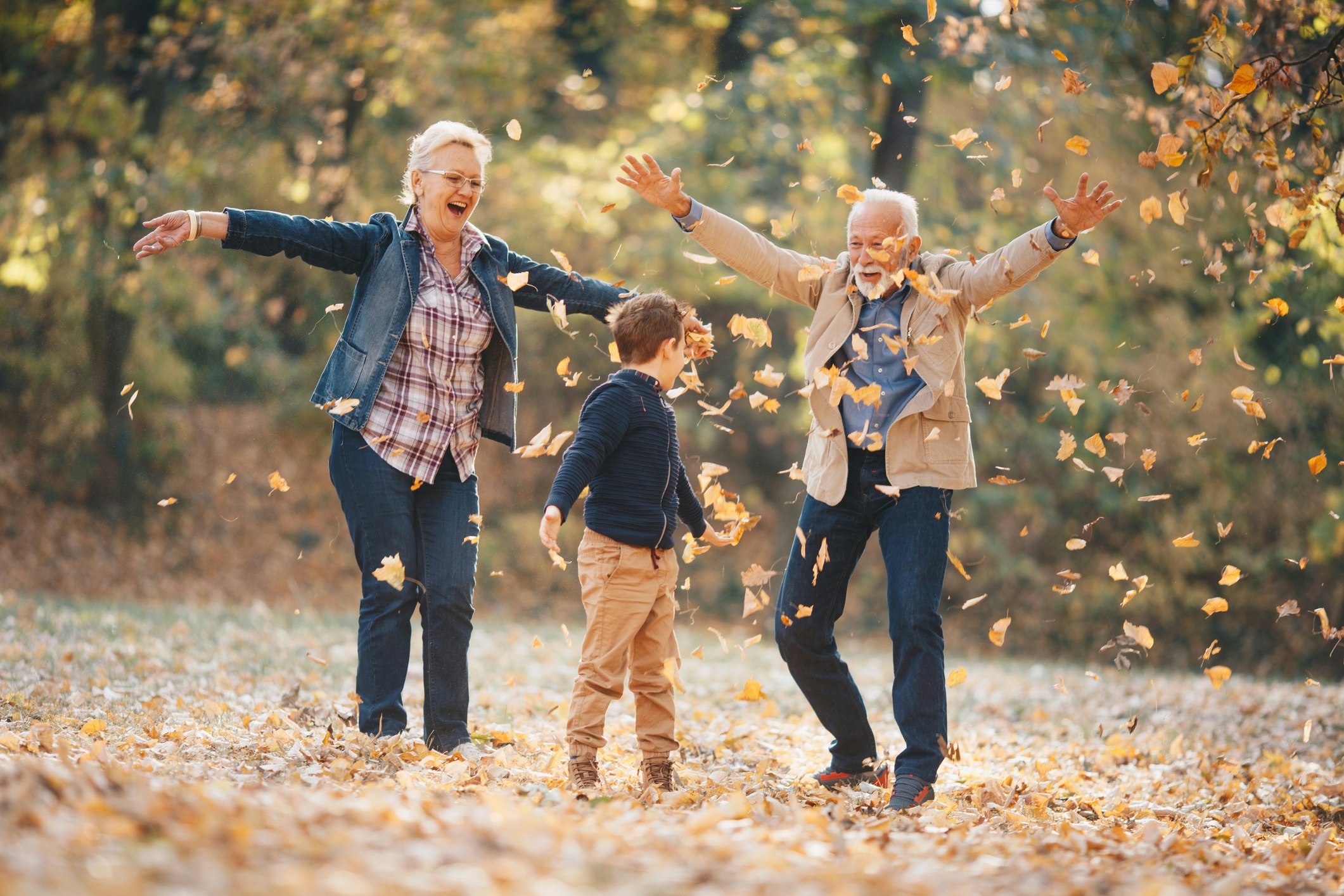 Grandparents playing in the leaves along with their grandson