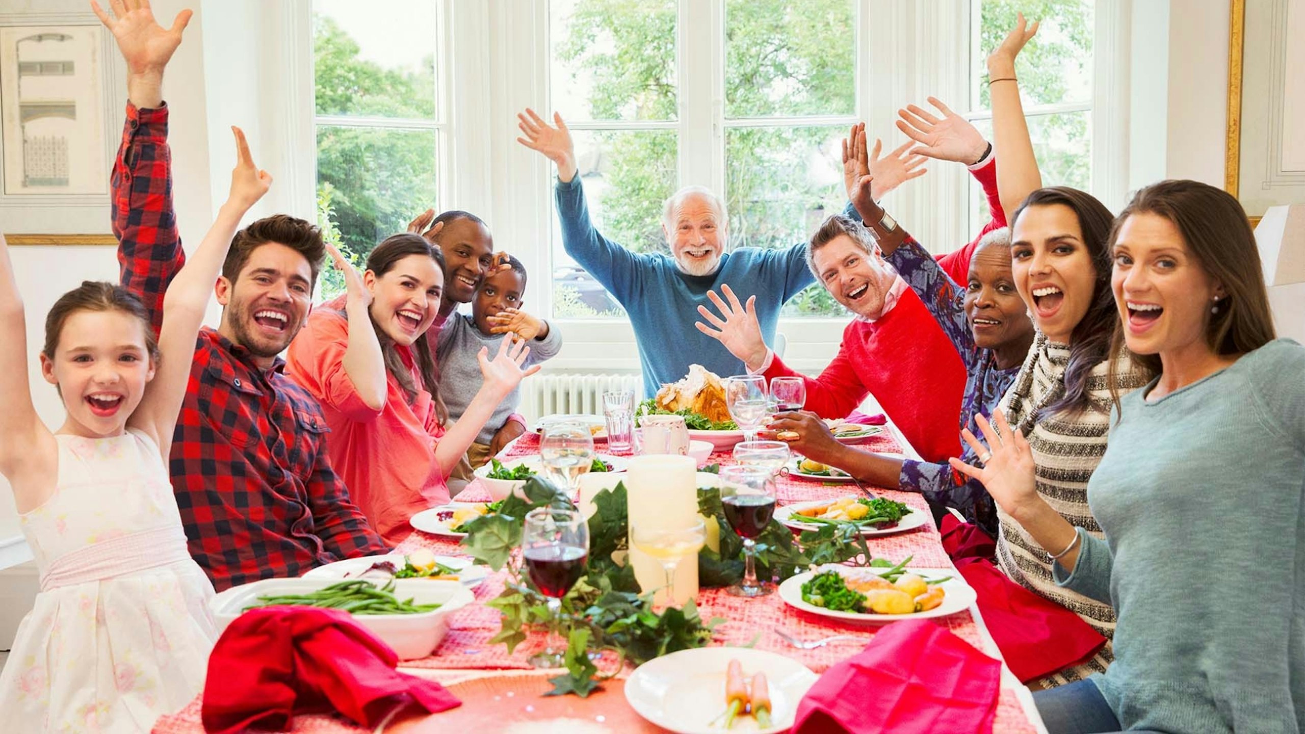 Portrait enthusiastic multi-ethnic multi-generation family waving at Christmas dinner table