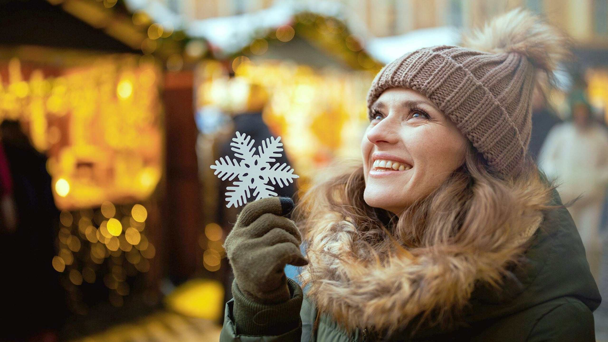 happy modern female in green coat and brown hat at the winter fair in the city with snowflake