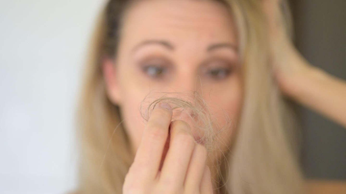 Woman looking at a loose tuft of hair after brushing it in consternation in a concept of middle-aged hair loss, focus on hand