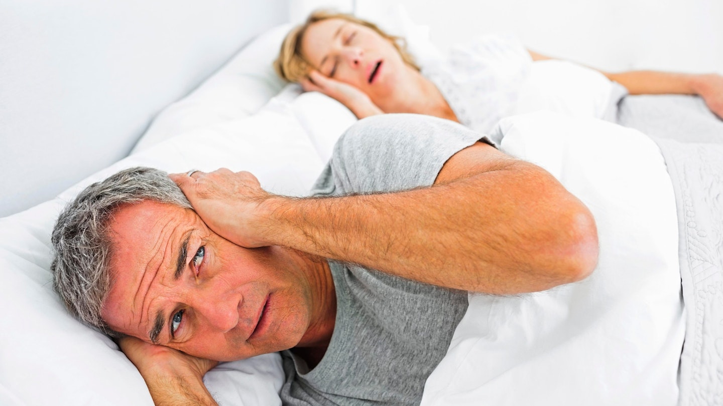 Fed up man blocking his ears from noise of wife snoring at home in bedroom