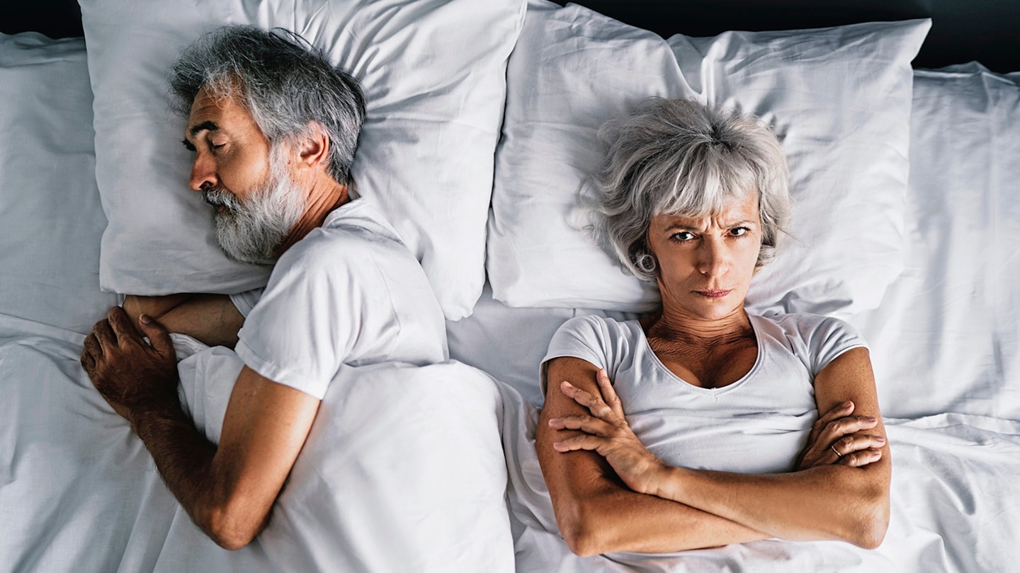 Overhead of senior couple in the bed. Pretty aged woman is angy with her sleeping husband