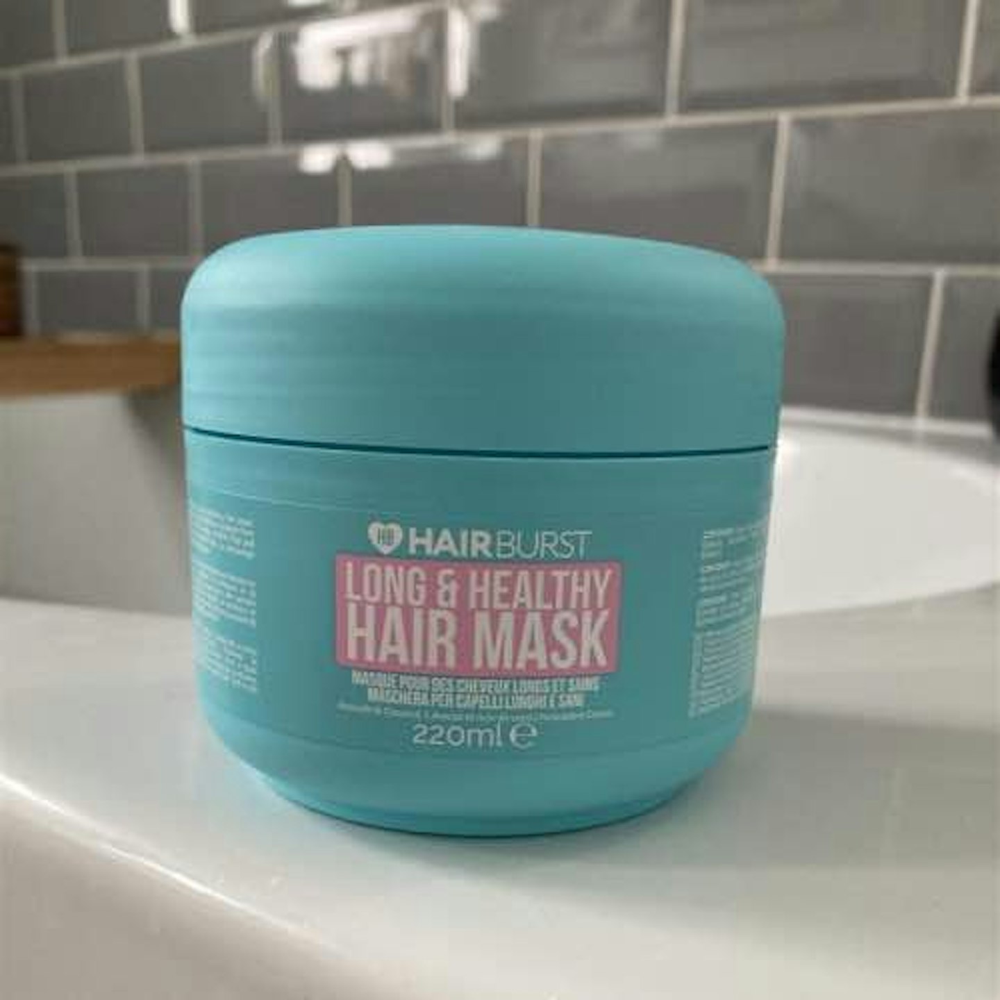 Hairburst long and healthy hair mask in turquoise tub with pink writing in a bathroom 
