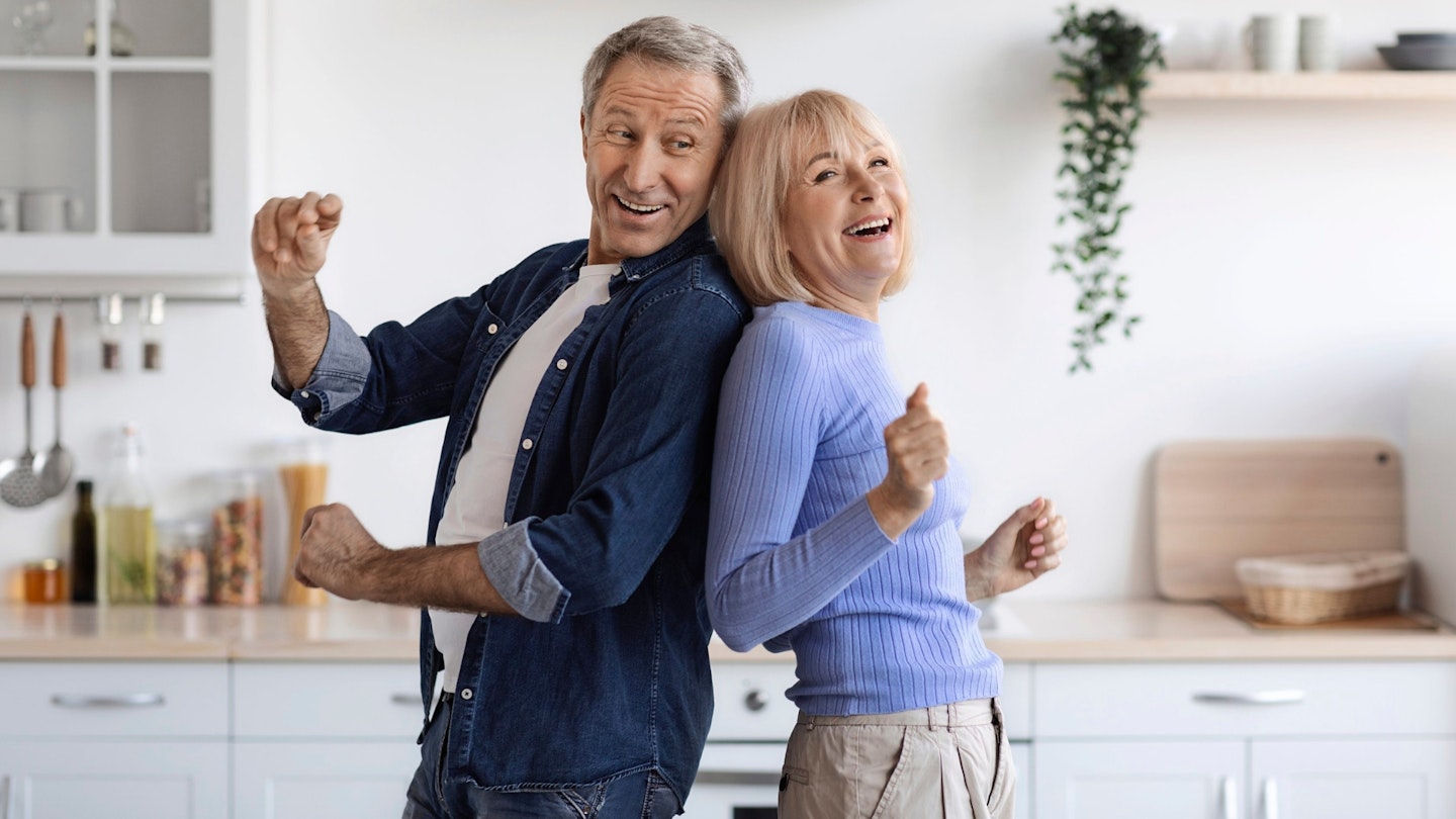 Joyful elderly spouses dancing together at kitchen