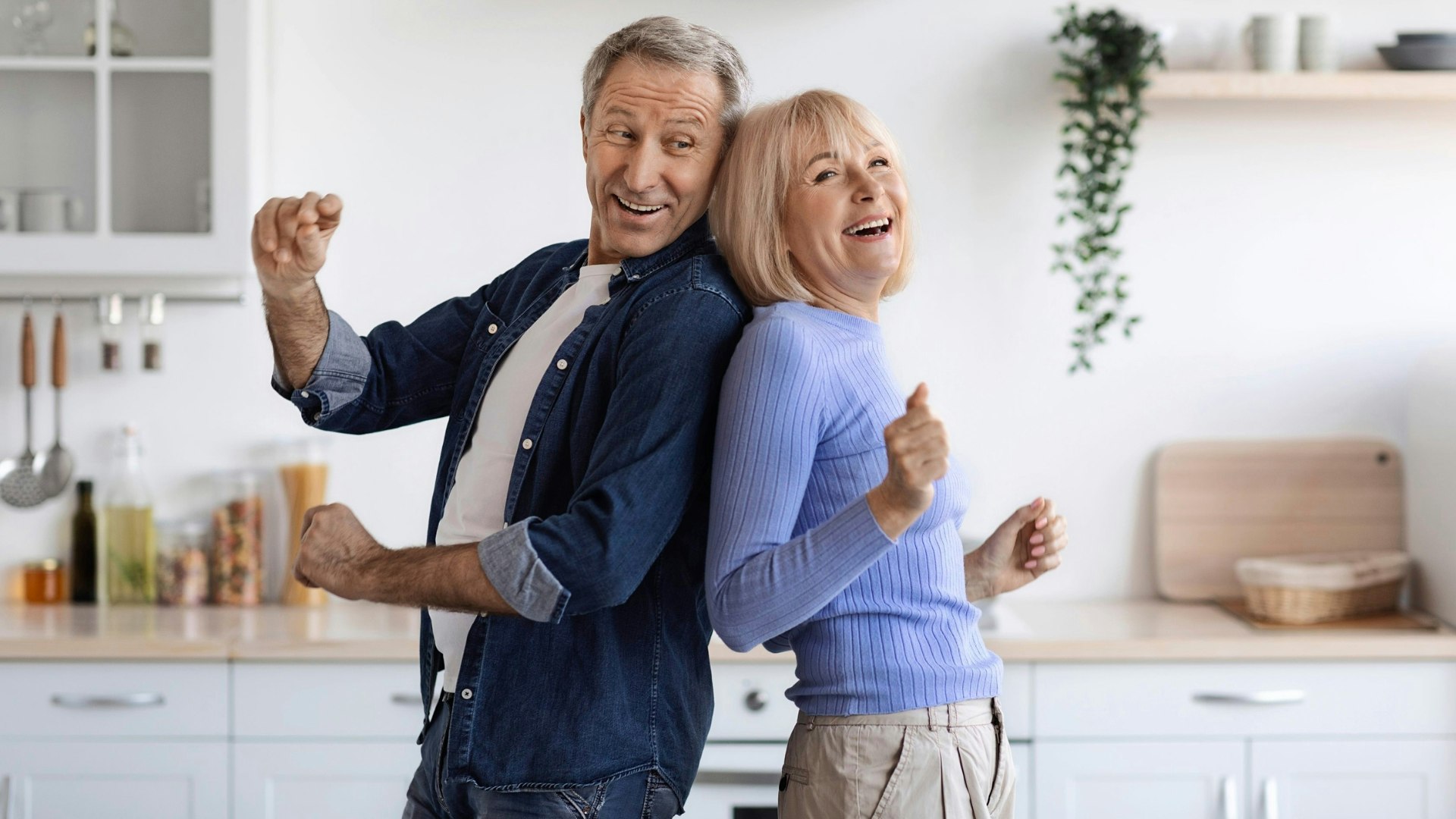 Joyful elderly spouses dancing together at kitchen
