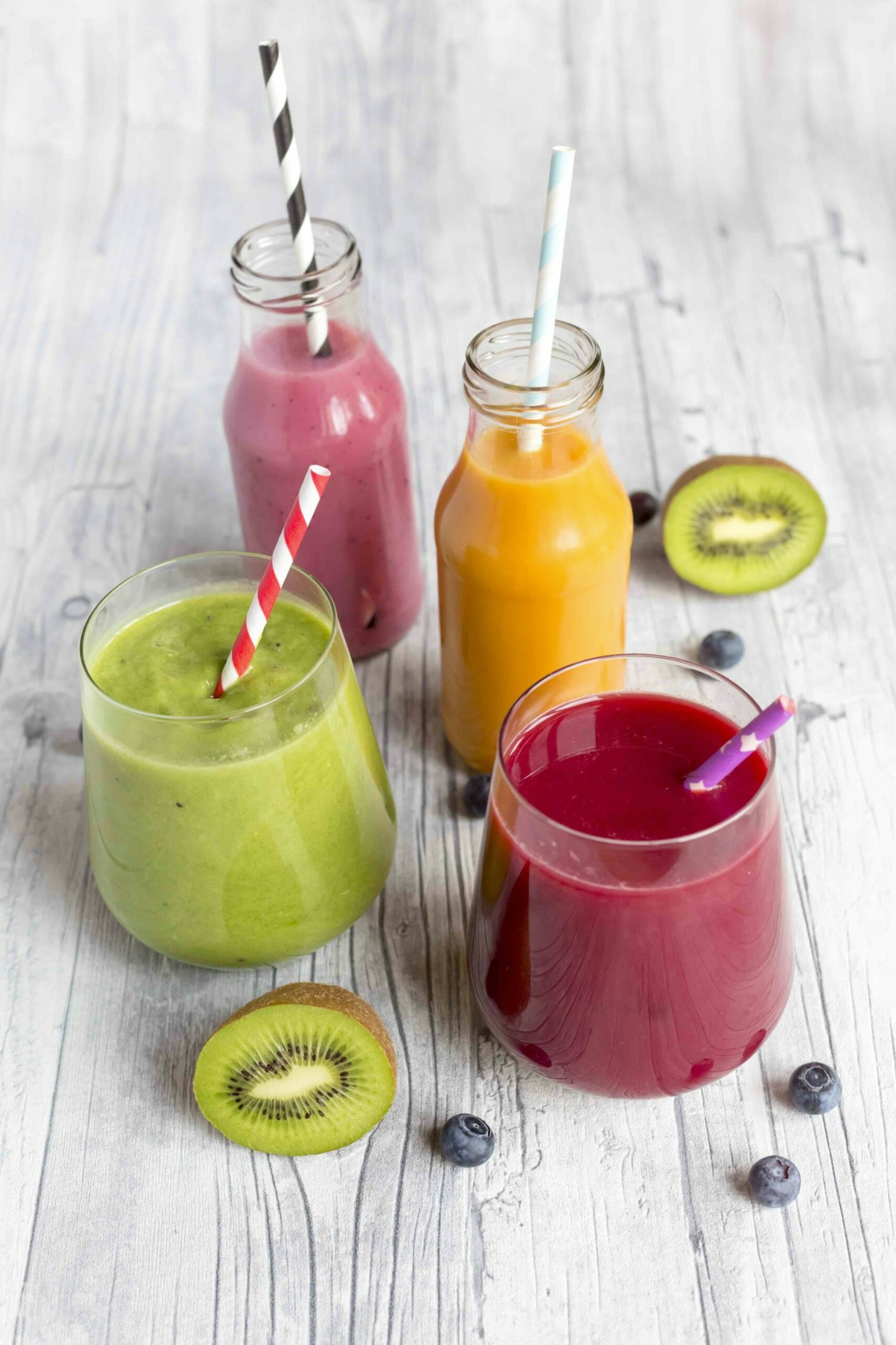 Glasses of four different smoothies and fruits on wood