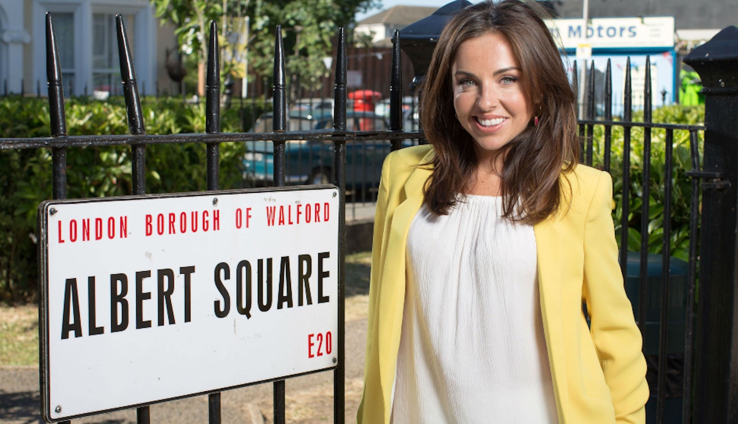 EastEnders actress Louisa Lytton as Ruby Allen posing next to the Albert Square sign