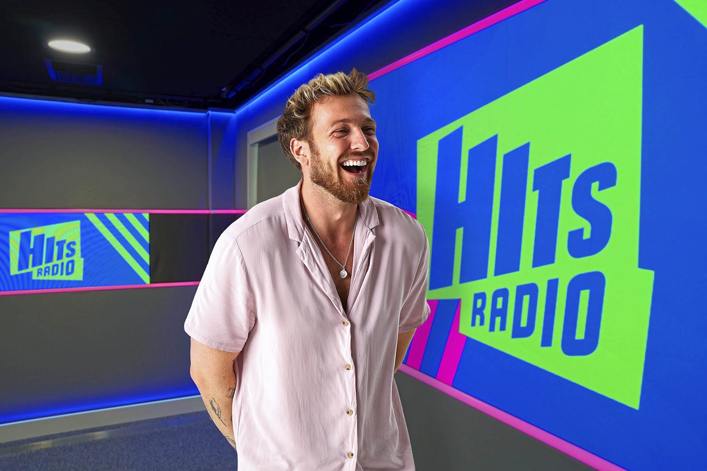 Sam Thompson looks happy stood in front of hits radio branding