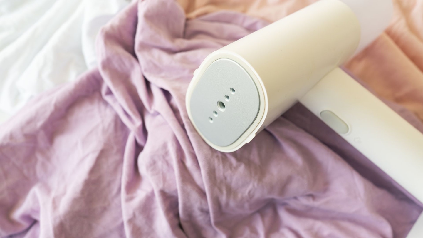 Handheld steamer rests on crumpled purple and white fabrics, ideal for quickly removing wrinkles