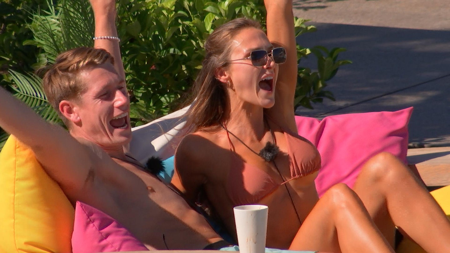 Will and Jessie sat on beanbags, cheering whilst in the villa