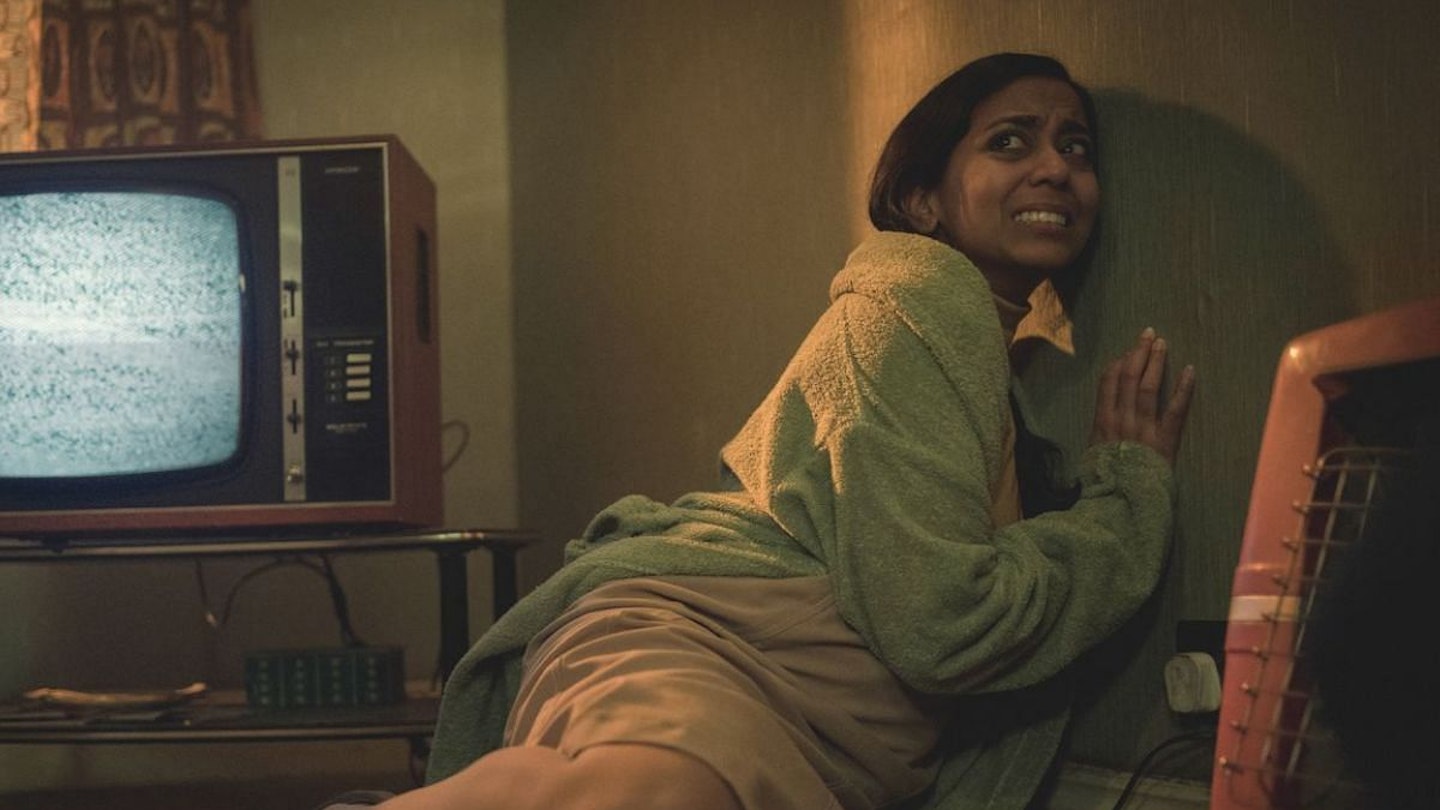 Anjana looking scared, huddled against a door from a scene of Black Mirror