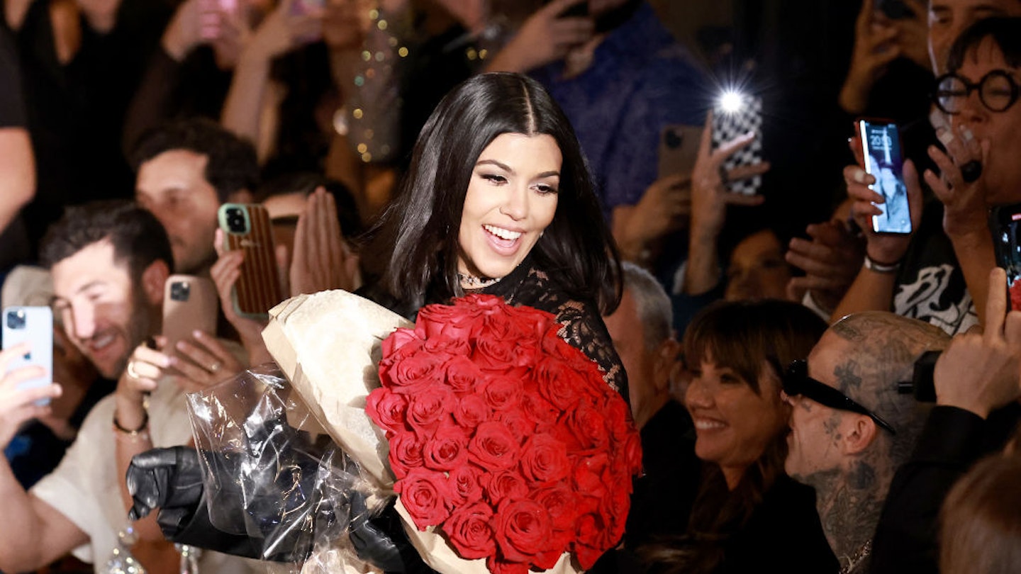 Kourtney holding roses and smiling during her Boohoo fashion show