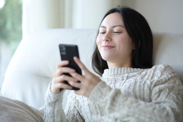 Satisfied asian woman checking cell phone on a sofa