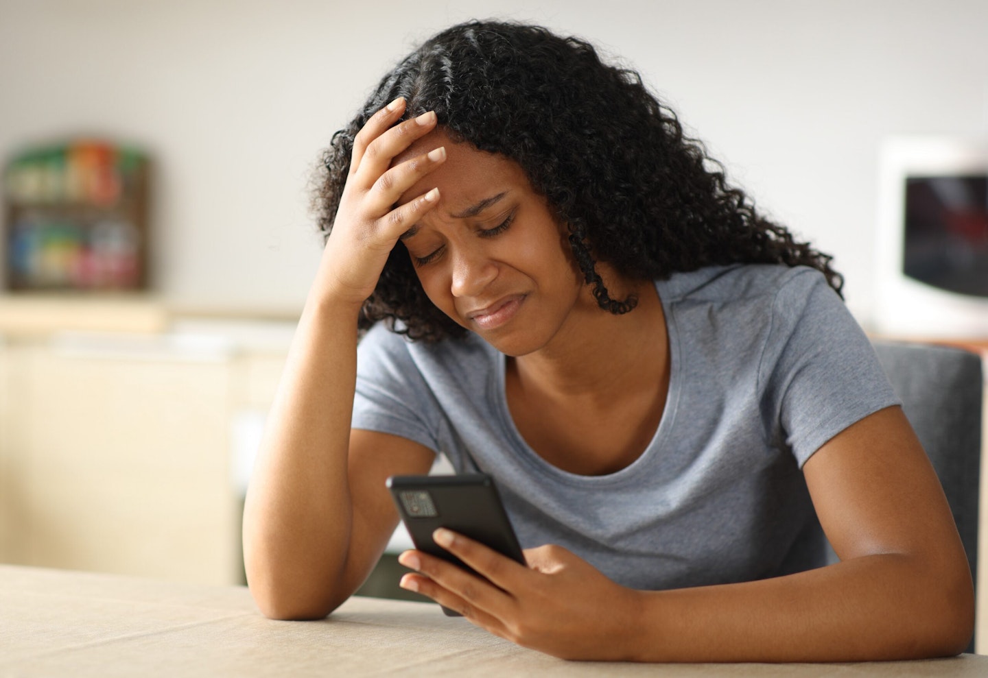 Sad woman checking phone in the kitchen at home