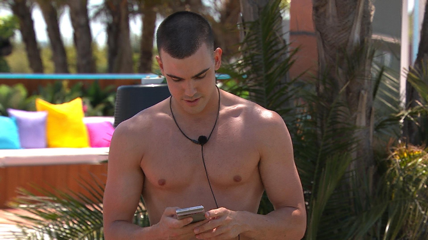 Shirtless clean-shaven Aaron getting a text in the Love Island villa