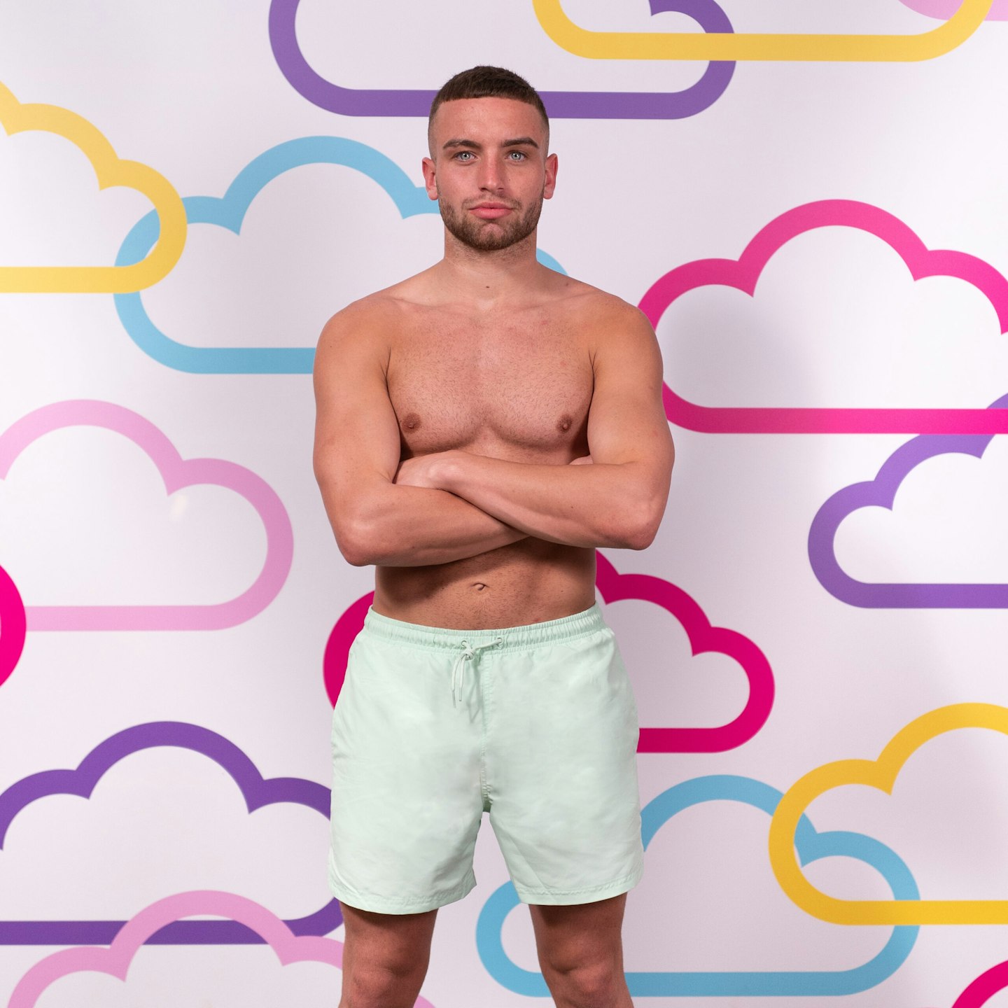 Kain Reed posing in front of a white background with multi-coloured clouds