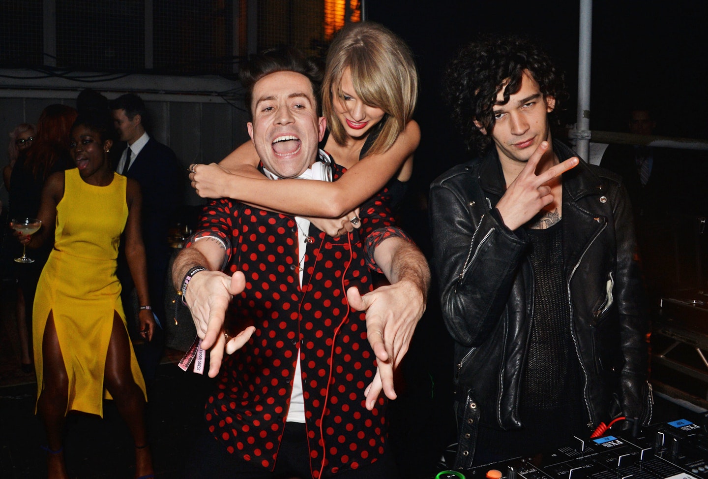 Taylor Swift hugging Nick Grimshaw while Matty Healy poses next to them
