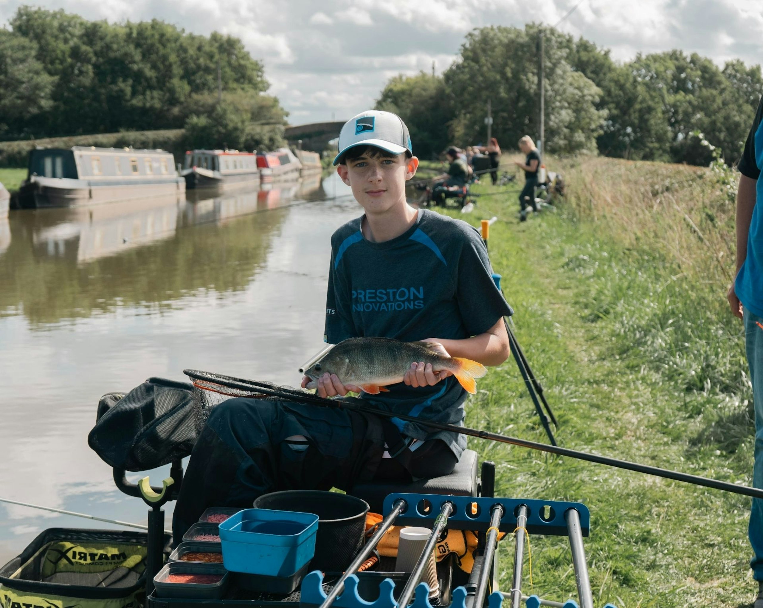 A young boy sat down holding his catch by the side of the river.