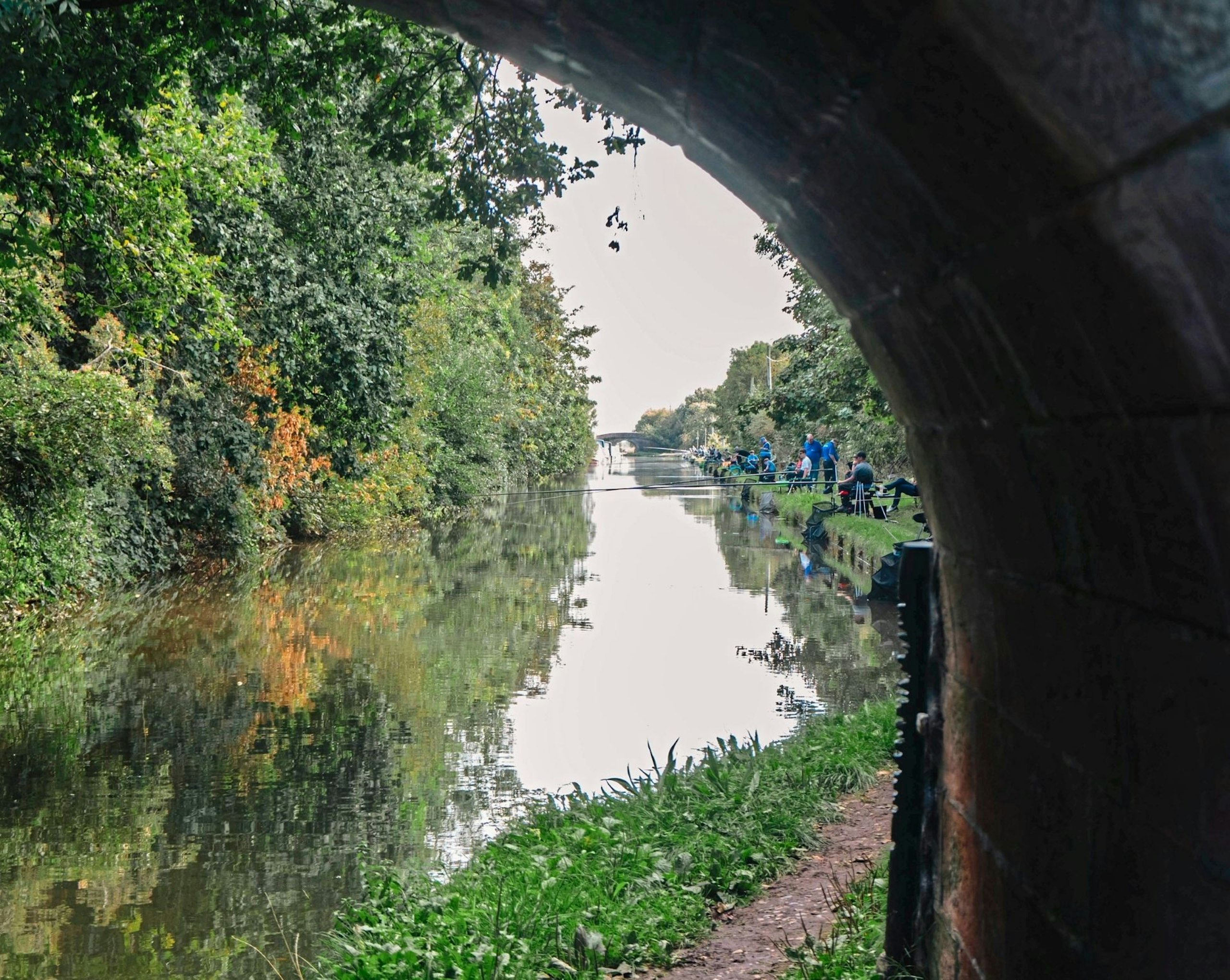 A lot of people along the side of the river fishing.