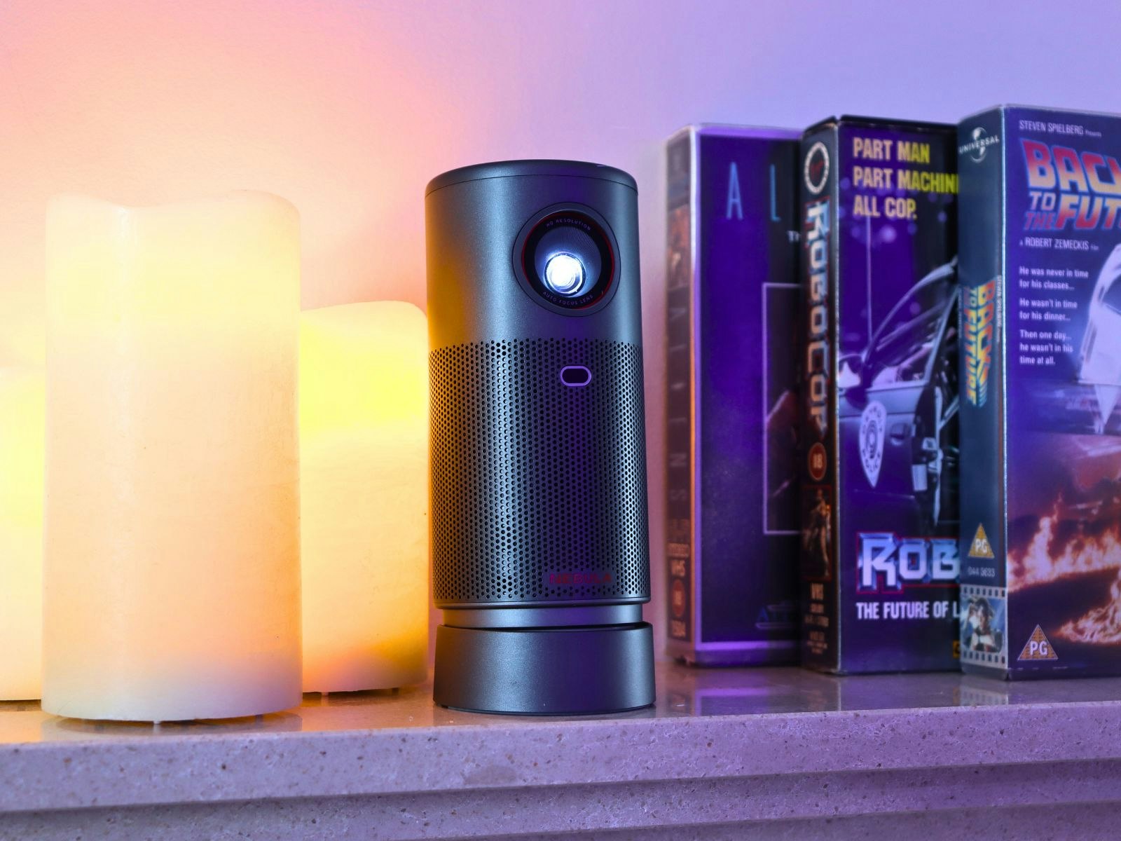 The Nebula Capsule Air projector on a shelf with candles and VHS movies