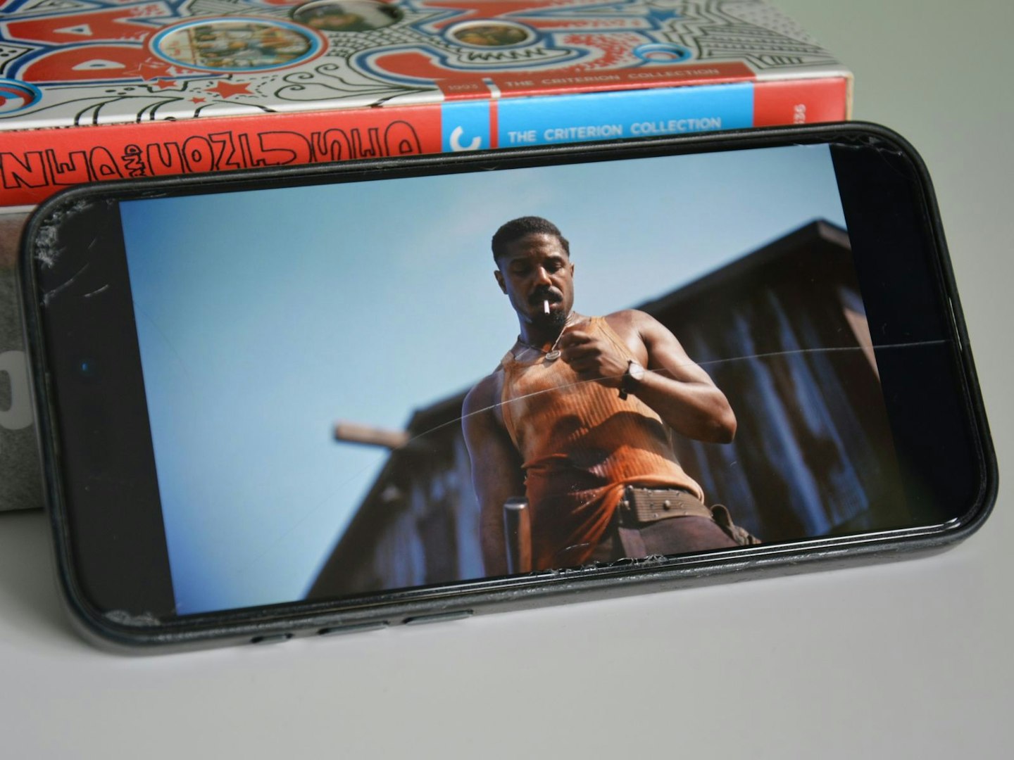 iPhone 15 Pro Max showing Ryan Coogler’s 2025 film Sinners via Apple TV, propped against an Oppenheimer book and Dazed and Confused Criterion 4K DVD