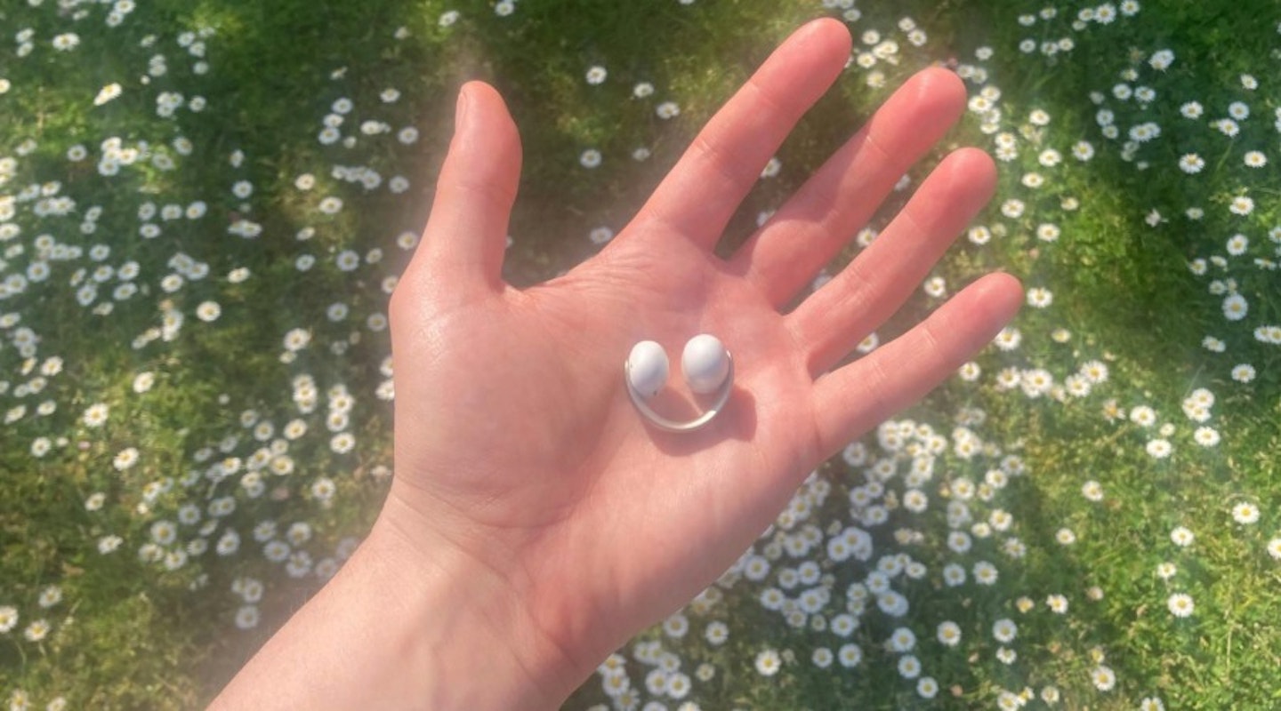 soundcore AeroClip open ear earbuds held in hand above grass with flowers. Best tech gifts for Christmas and beyond.