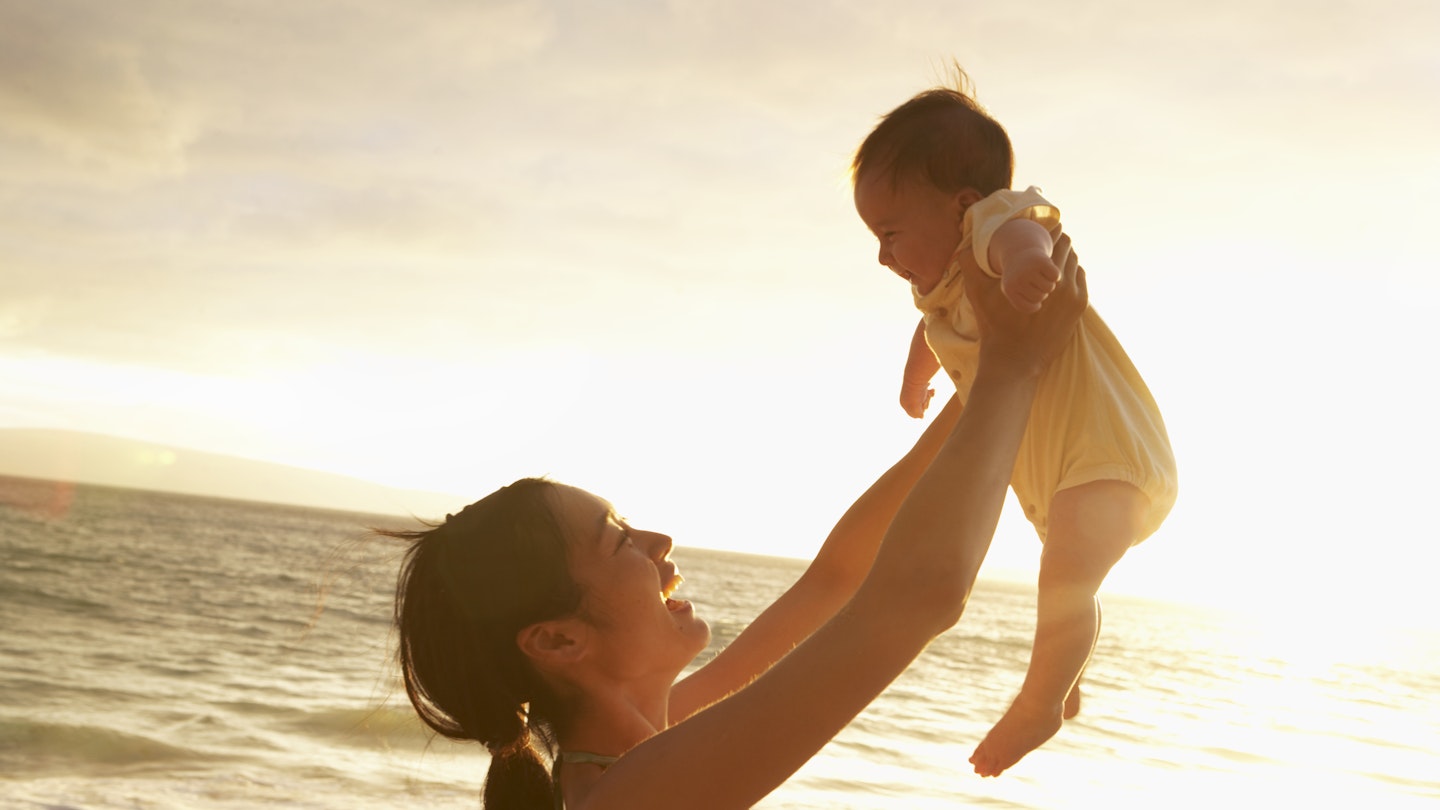 Woman holding baby up against a sunset