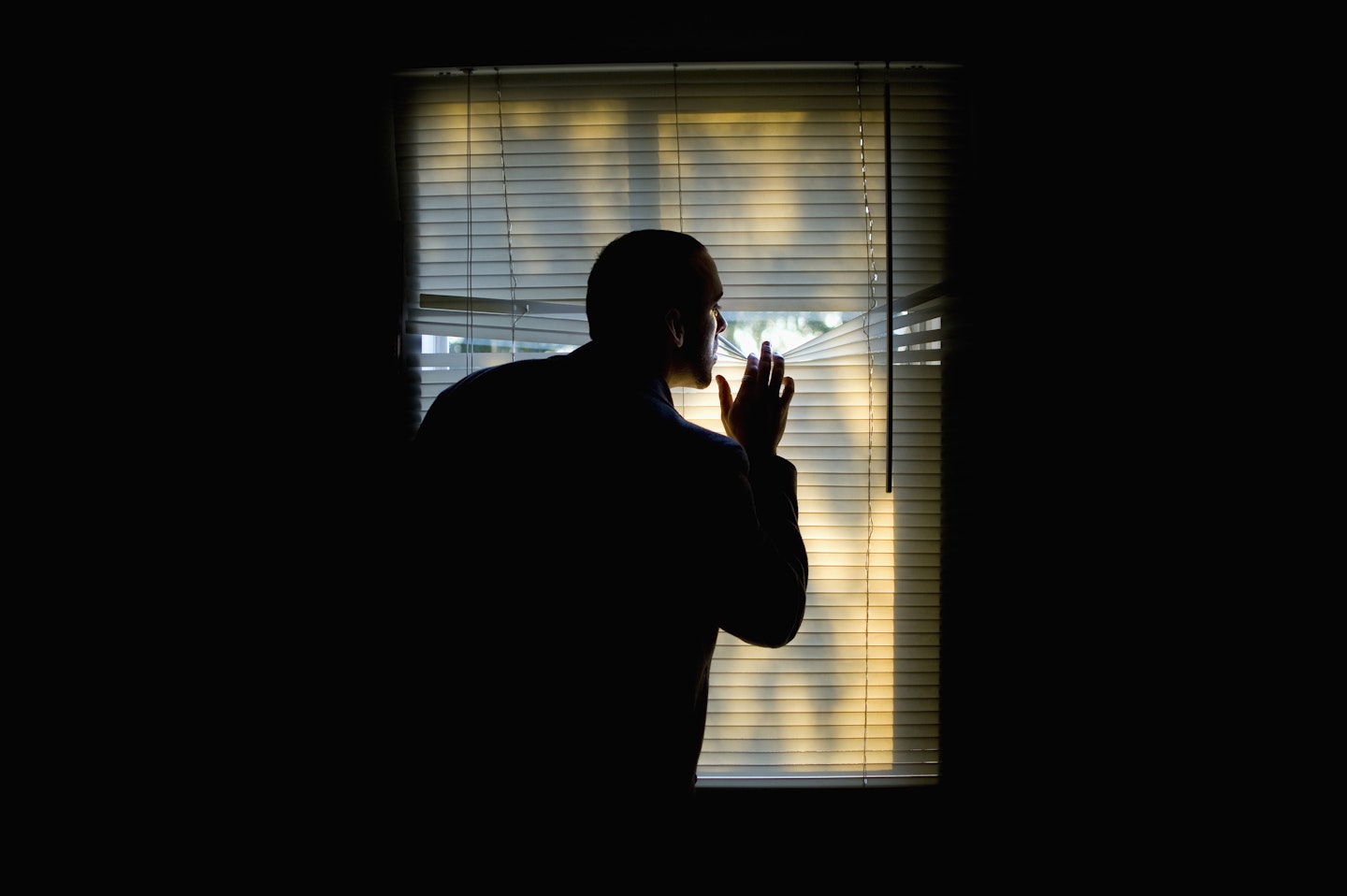 Silhouette of man peers out of window