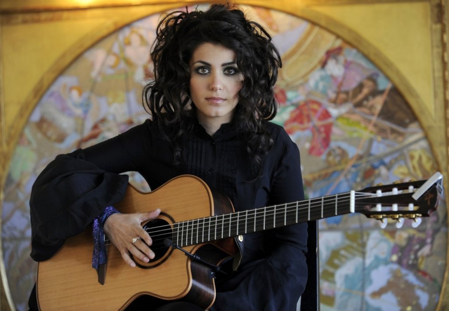 Katie Melua standing looking into the camera whilst holding her guitar