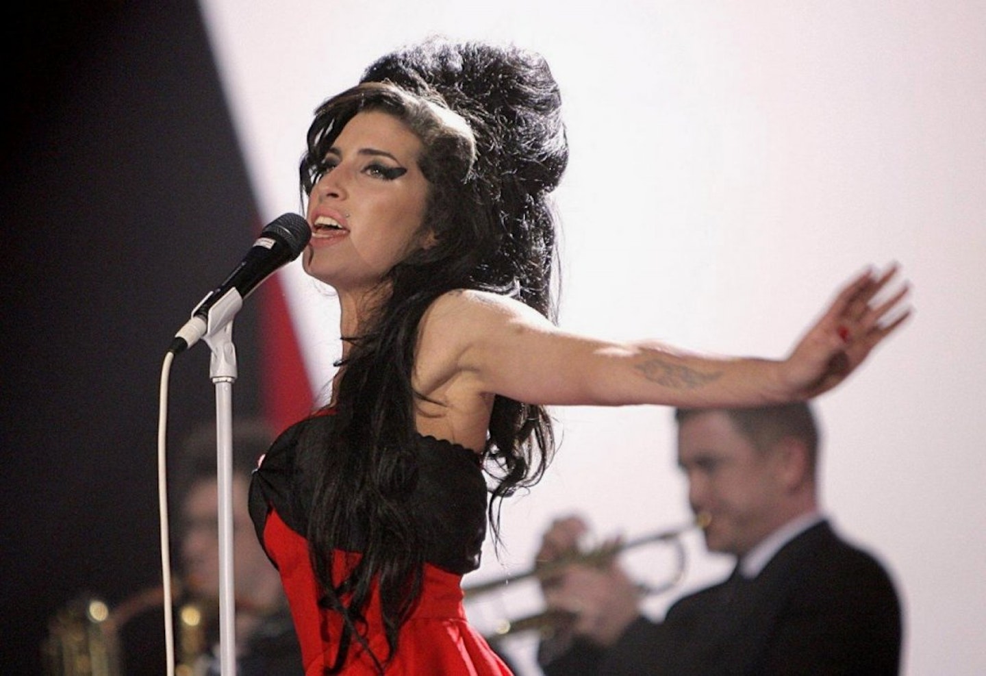 Amy Winehouse singing on stage in a red and black dress