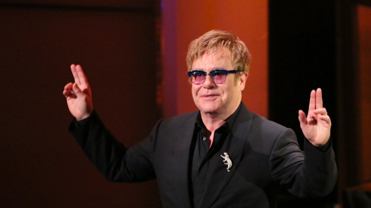 Elton John in a black suit and pink glasses