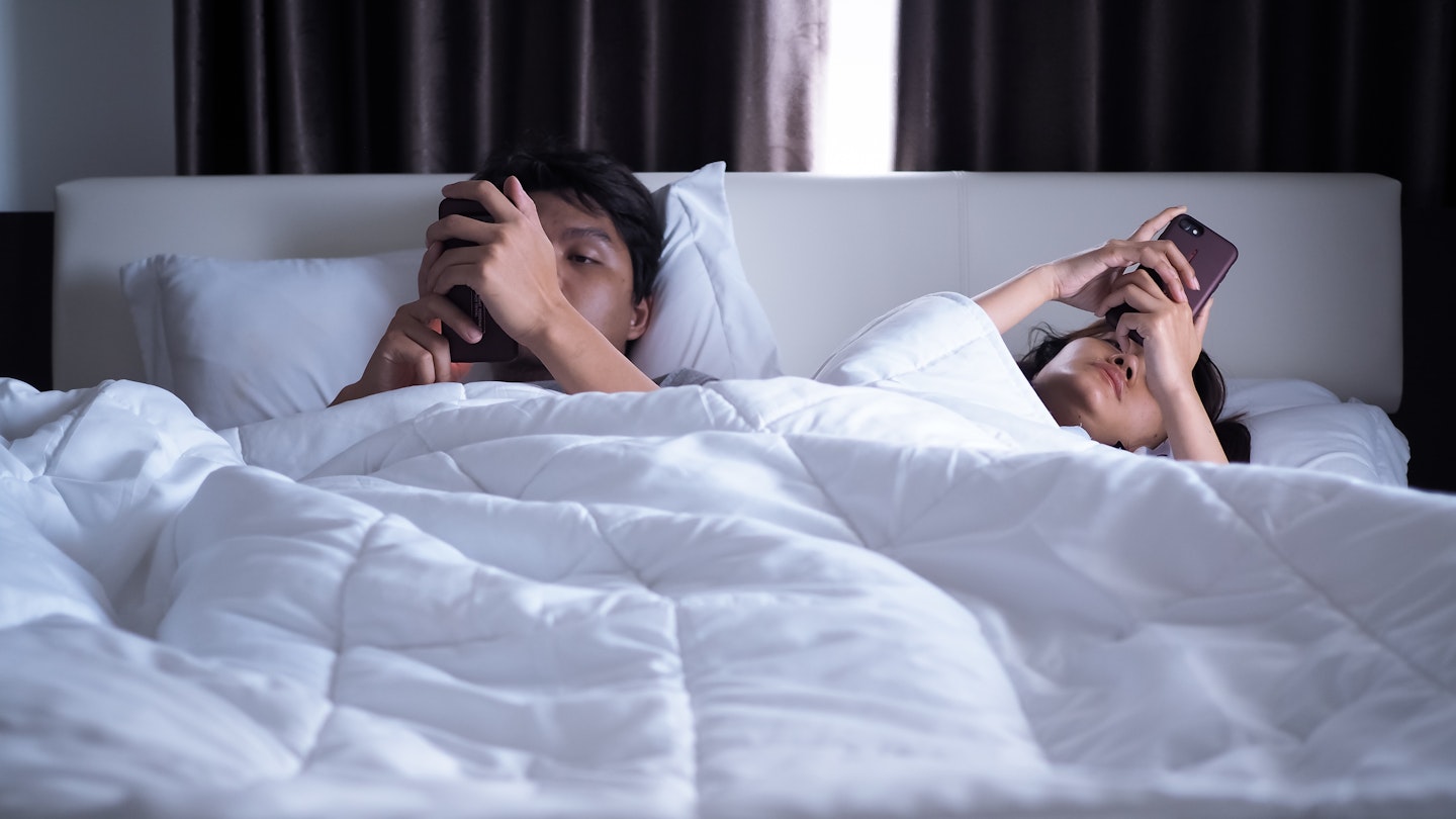 Two people in bed looking at their phones