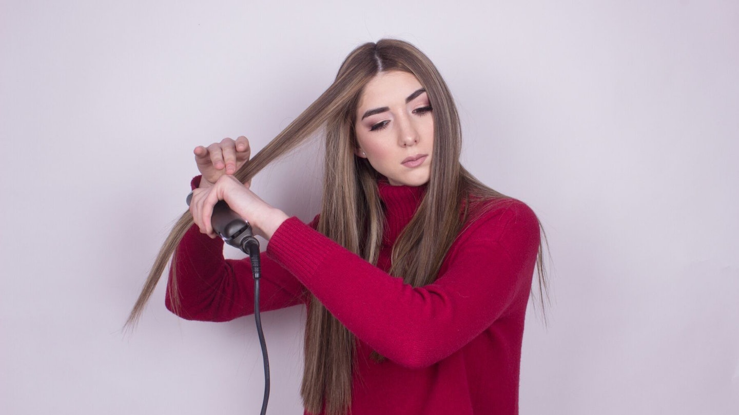 Young woman straightening her long hair
