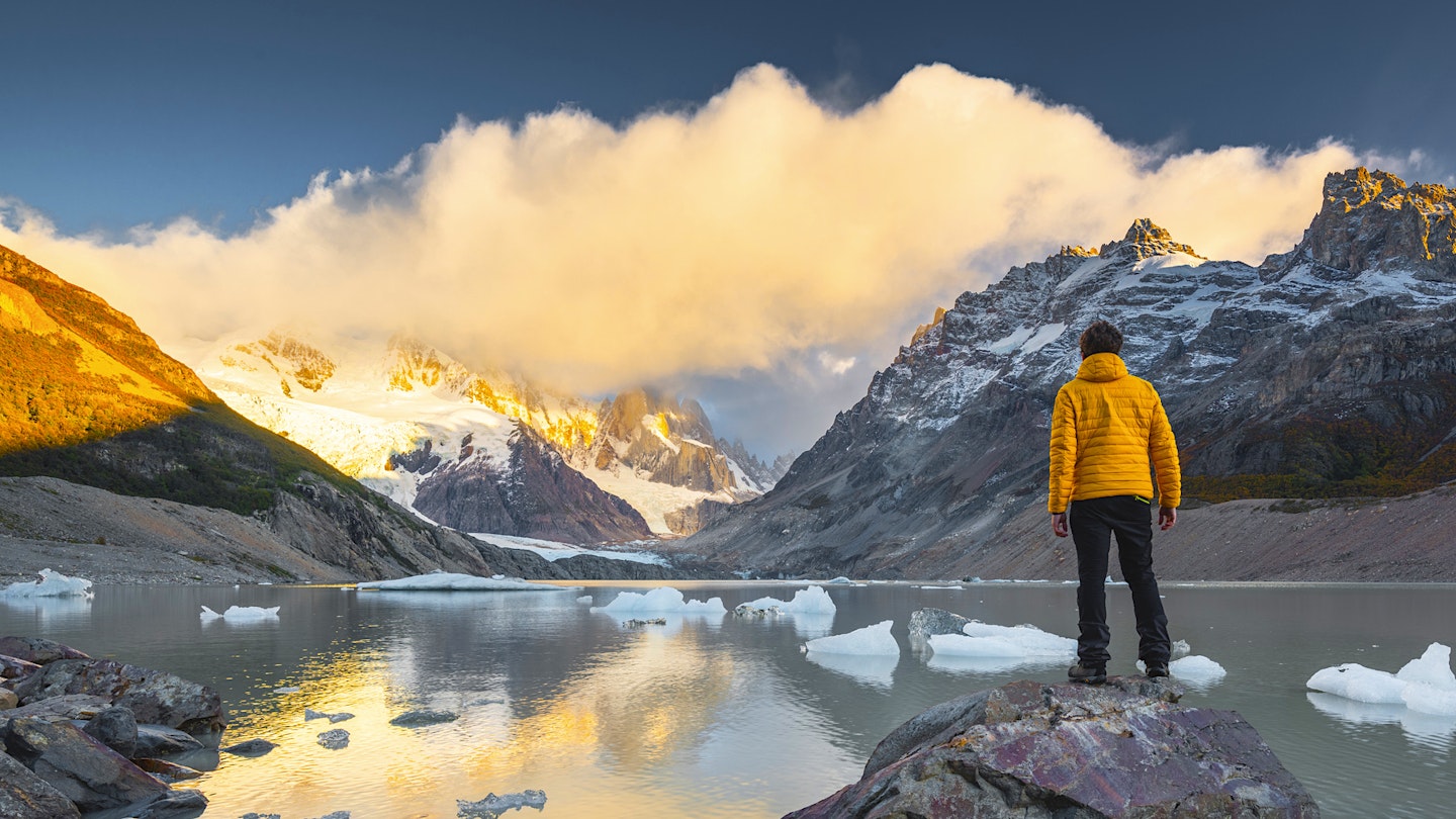 Person in down jacket looks a snowy mountain in front of a lake