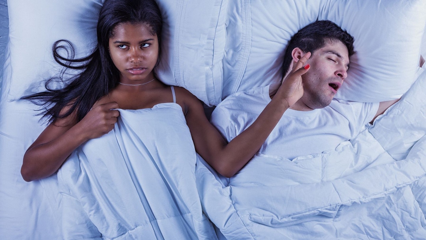 Young couple in bed, woman annoyed at man snoring