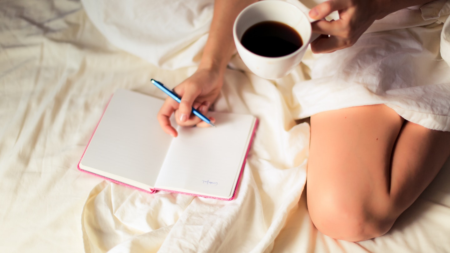 Woman journaling on bed with cup of coffee
