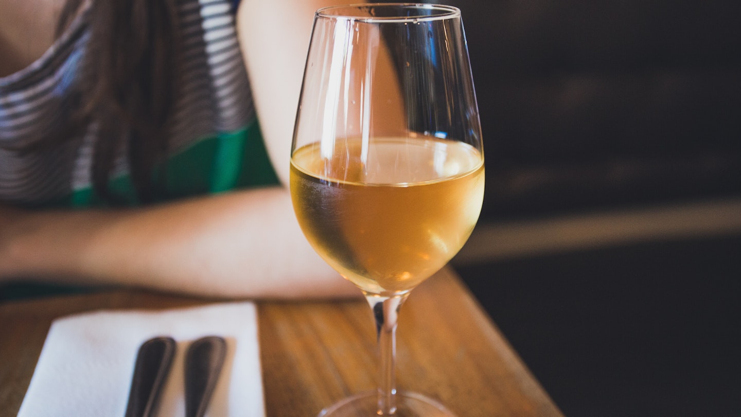 Glass of white wine on table and woman in background