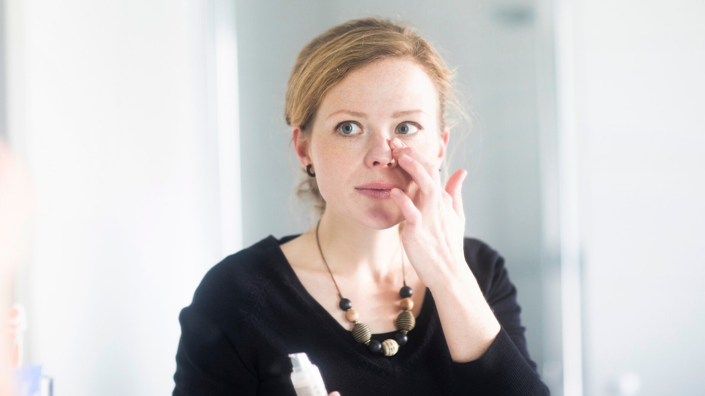 Young woman applying eye cream in the mirror