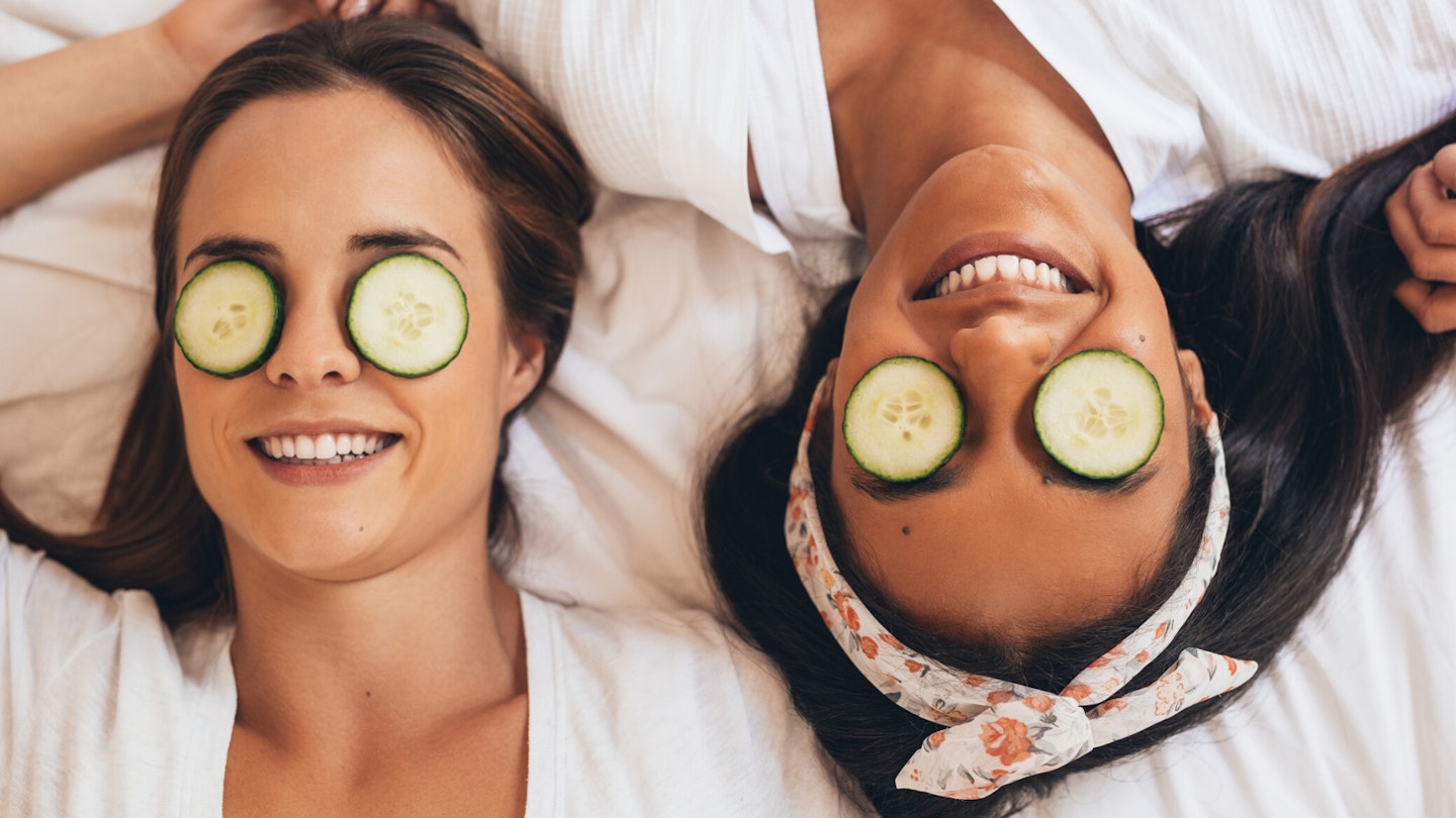 Two women led on bed with cucumber on eyes