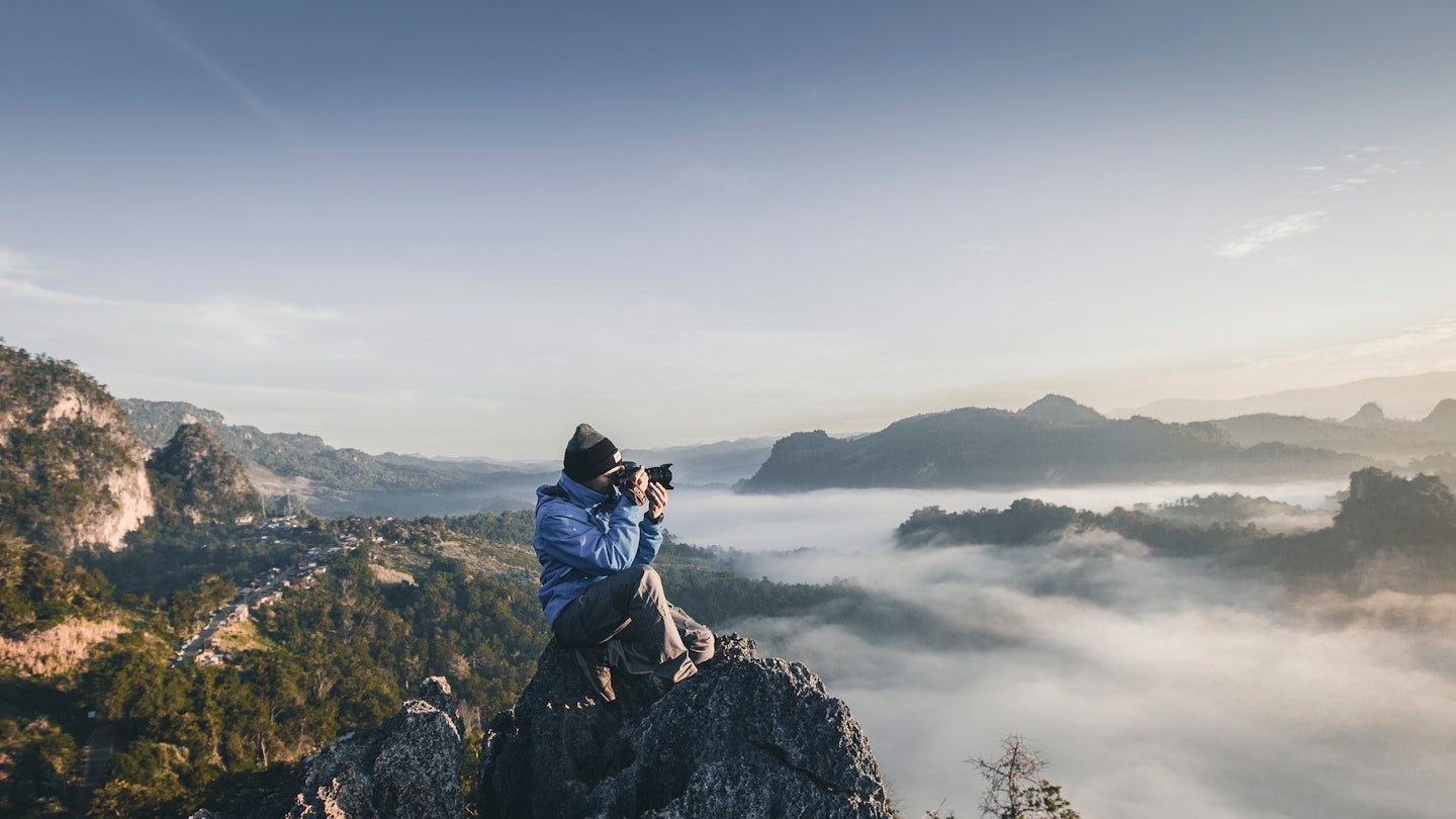 Adventure photographer perched on a rock taking a photograph of the landscape