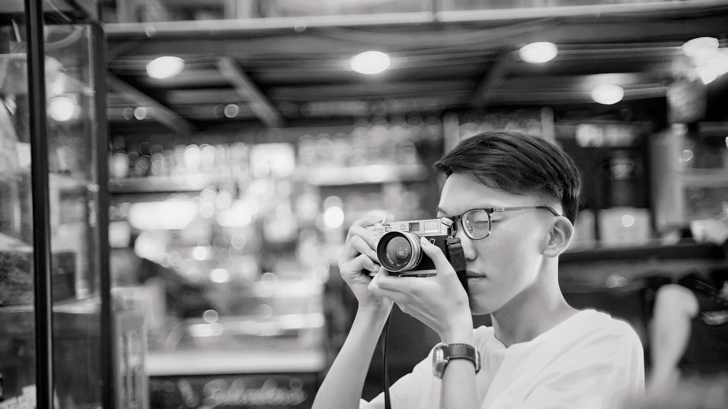 Black and white image of a young man taking a photograph indoors