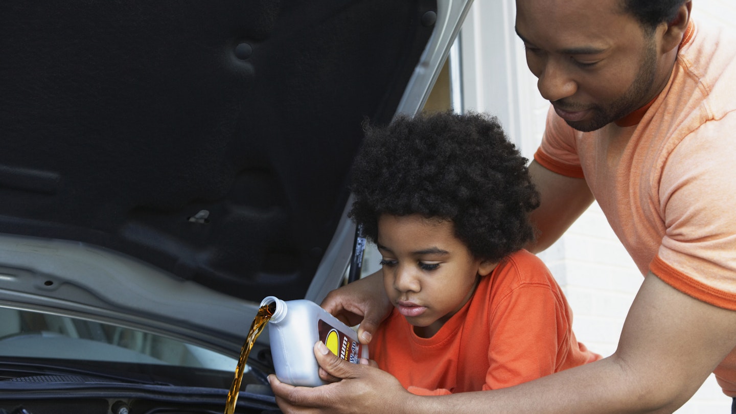 A man and child add oil to their car's engine